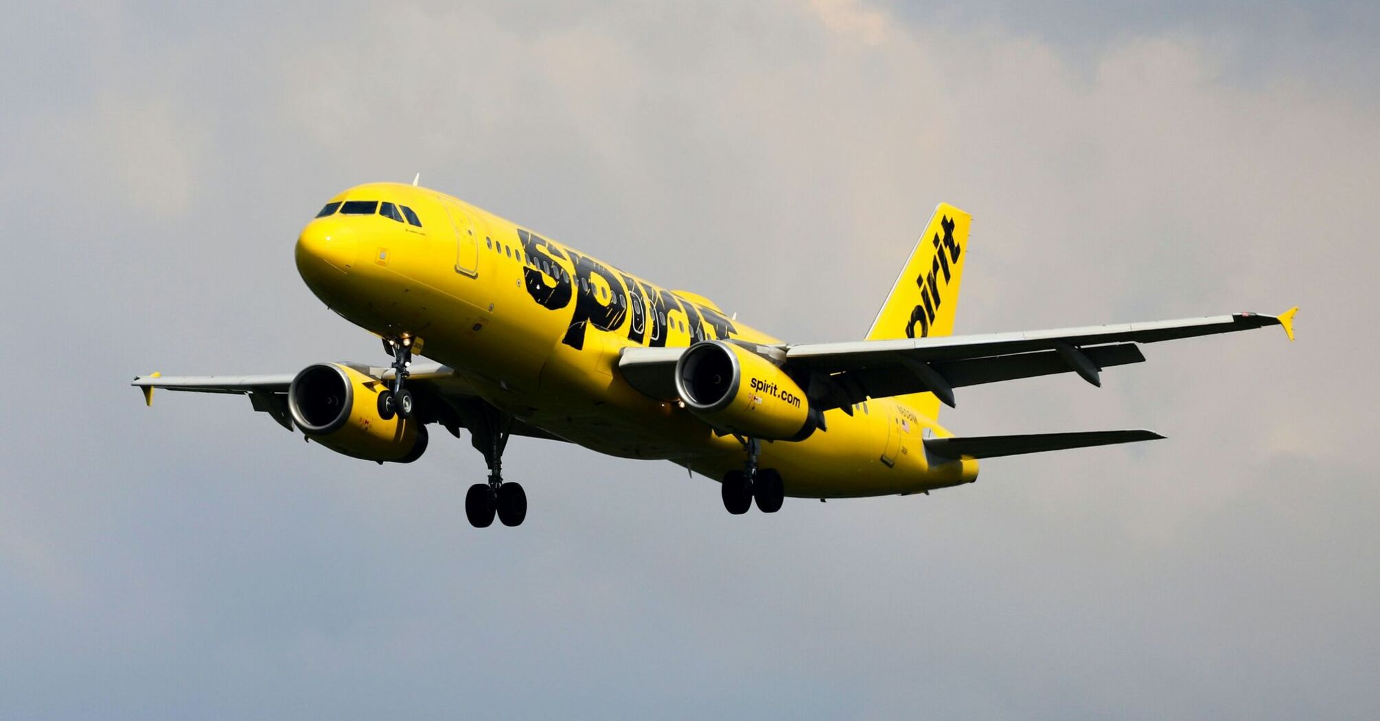 A yellow and black Spirit airplane flying