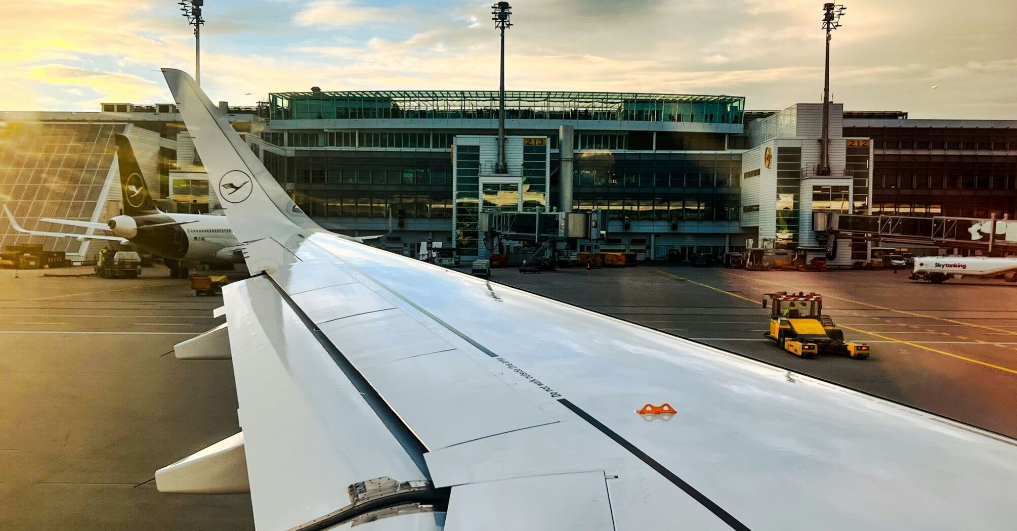 The wing of an airplane with an airport building in the background