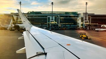 The wing of an airplane with an airport building in the background
