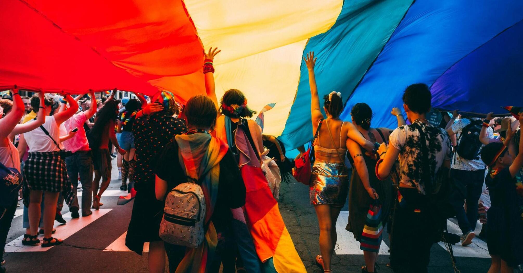 People running forward under a rainbow flag