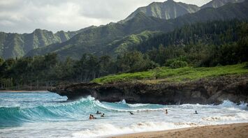 Scenic beach with people swimming and lush green mountains in the background