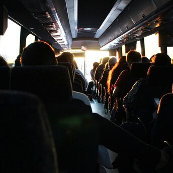 Passengers seated in a motorcoach, sunlight streaming through the front window