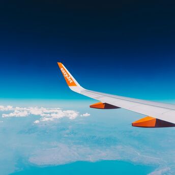 View from an easyJet airplane window showing wing and orange logo against a backdrop of blue skies and distant landscapes below