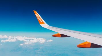 View from an easyJet airplane window showing wing and orange logo against a backdrop of blue skies and distant landscapes below