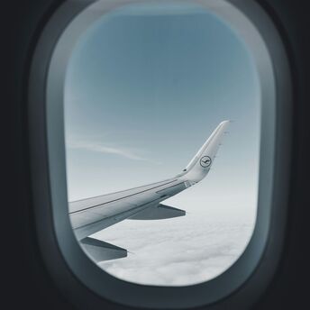 View through an airplane window showing the wing of a Lufthansa aircraft flying above the clouds