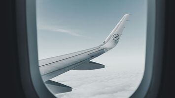 View through an airplane window showing the wing of a Lufthansa aircraft flying above the clouds