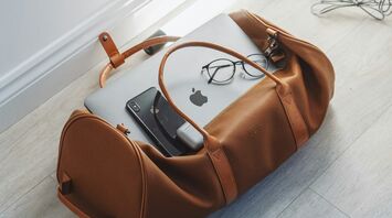 Travel bag with a laptop, smartphone, and eyeglasses inside, lying on a wooden floor