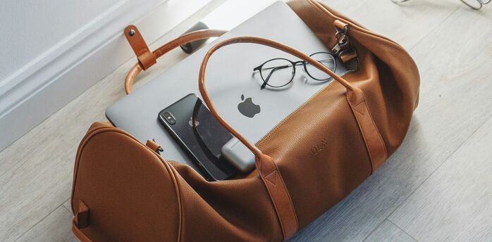 Travel bag with a laptop, smartphone, and eyeglasses inside, lying on a wooden floor