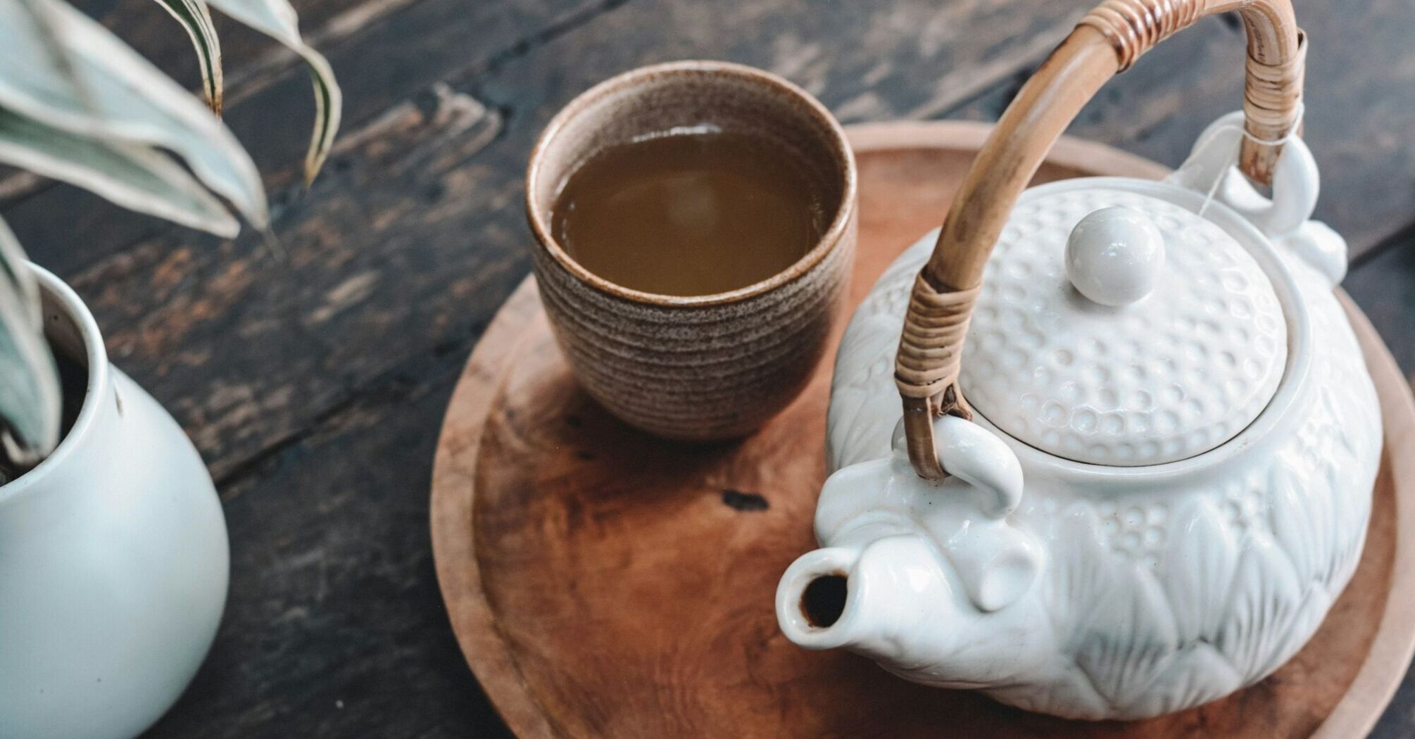 A ceramic teapot and cup of tea on a wooden tray