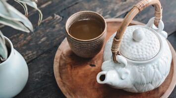 A ceramic teapot and cup of tea on a wooden tray