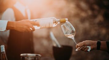 Person pouring white wine into a glass outdoors