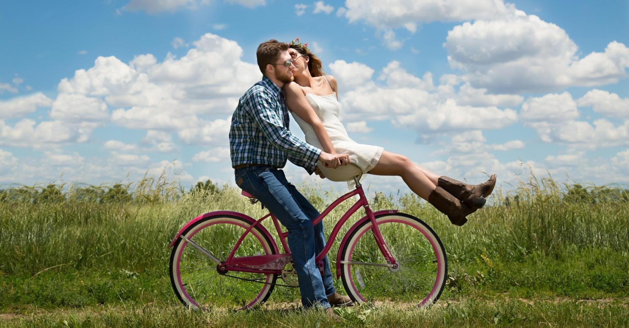 Couple is riding a bicycle in a field