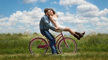 Couple is riding a bicycle in a field