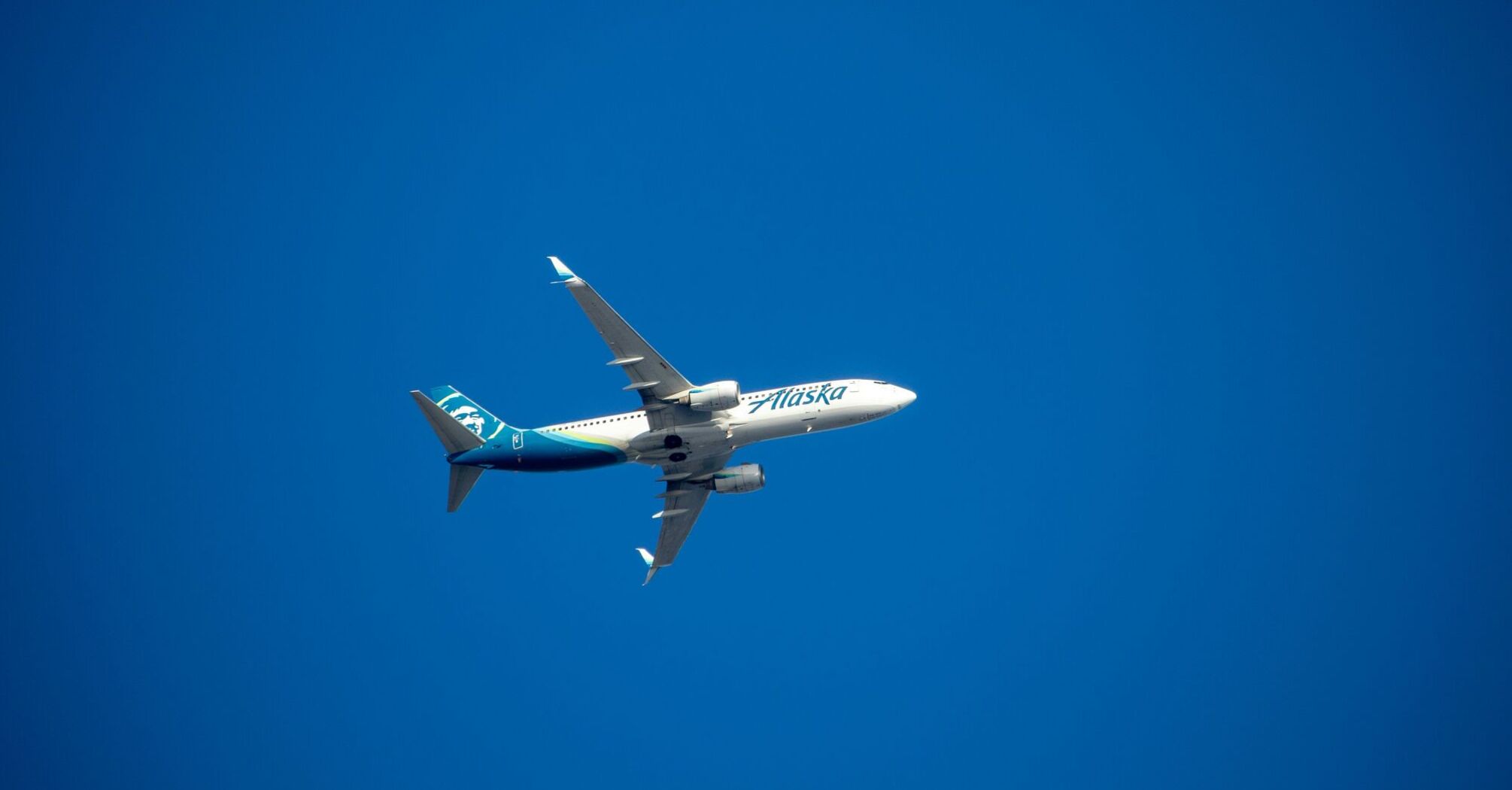 A blue and white Alaska Airlines airplane flying in a blue sky