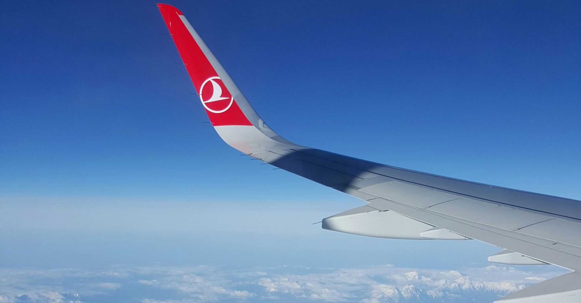 Turkish Airlines airplane wing flying over snow-capped mountains