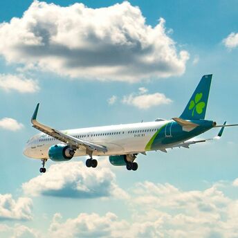 An Aer Lingus Airbus A330-300 aircraft in flight against a backdrop of clouds and blue sky