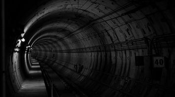 A dark, empty railway tunnel with light fixtures on the wall