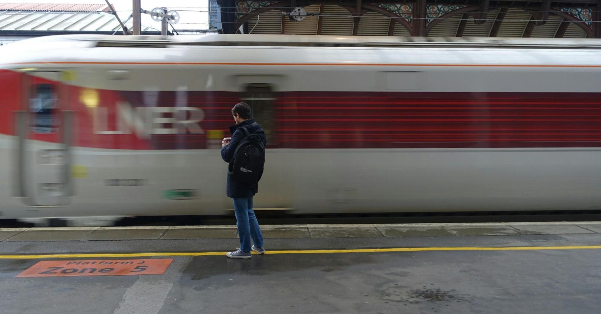 A man standing on a station in front of a LNER train