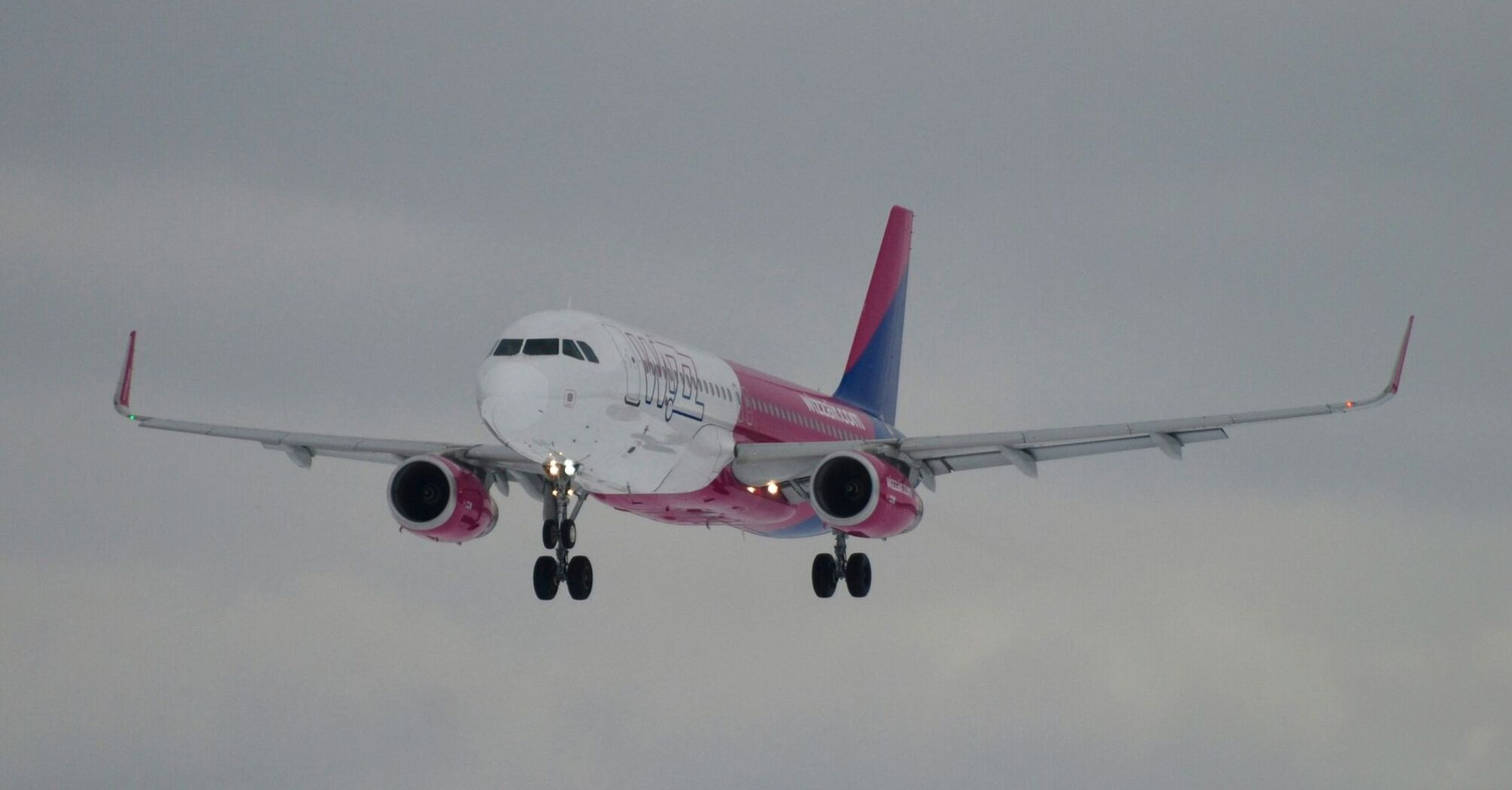 A large Wizzair jetliner flying through a cloudy sky