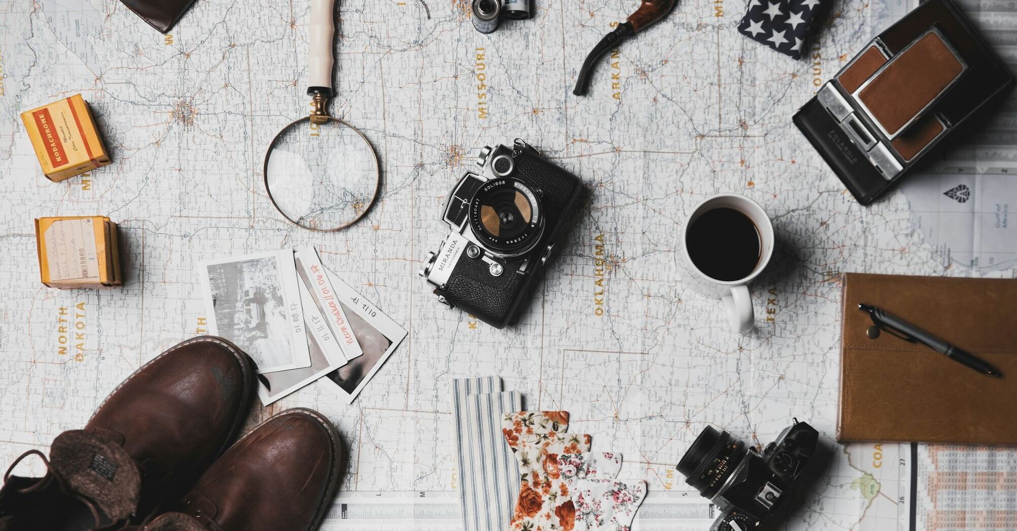 Travel essentials including camera, maps, and coffee on a table