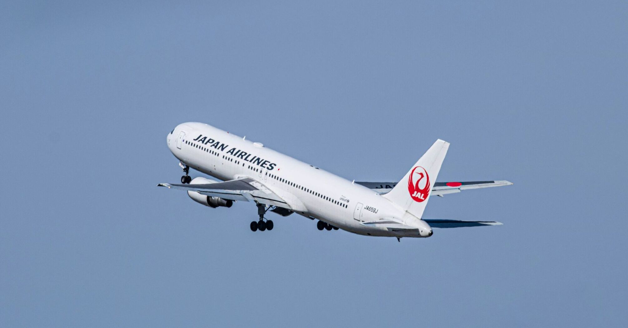 A large japan airlines jetliner flying through a blue sky
