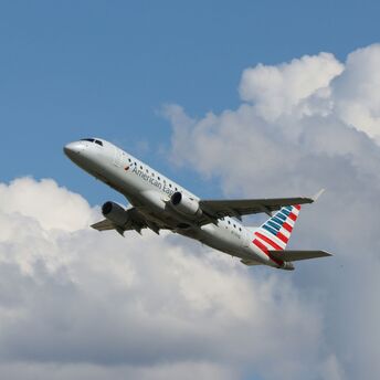 a large American Airlines passenger jet flying through a cloudy blue sky