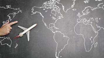 Hand pointing to a toy airplane on a world map drawn on a chalkboard