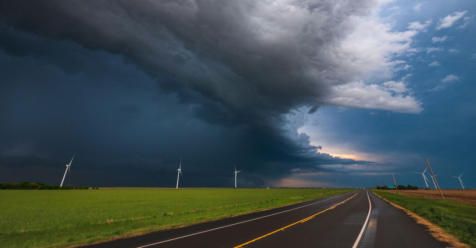 Dark storm clouds over a rural road and wind turbines