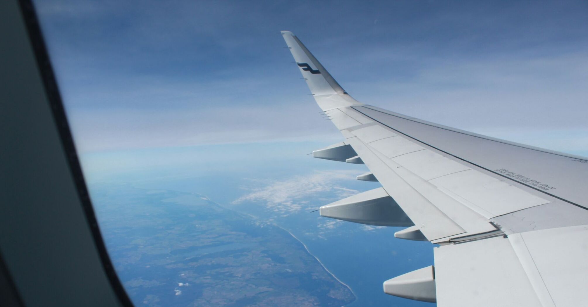 A view from an airplane window showing a Finnair wing and the coastline below