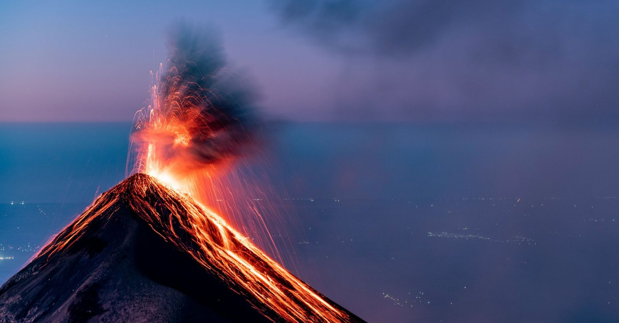 Eruption of a volcano with glowing lava and ash plume at dusk