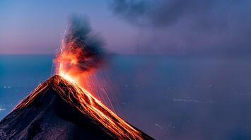 Eruption of a volcano with glowing lava and ash plume at dusk