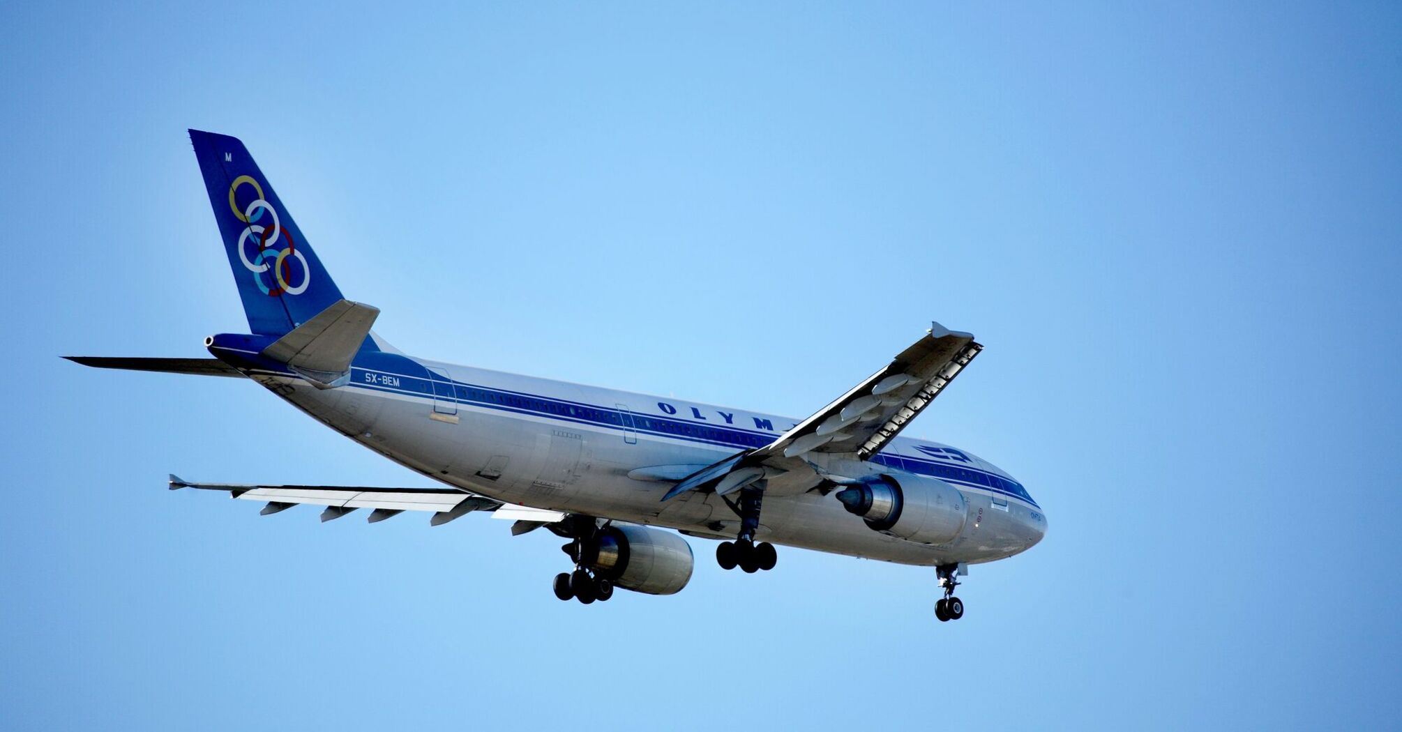 a blue and white Olympic Airways jet airliner flying in the sky