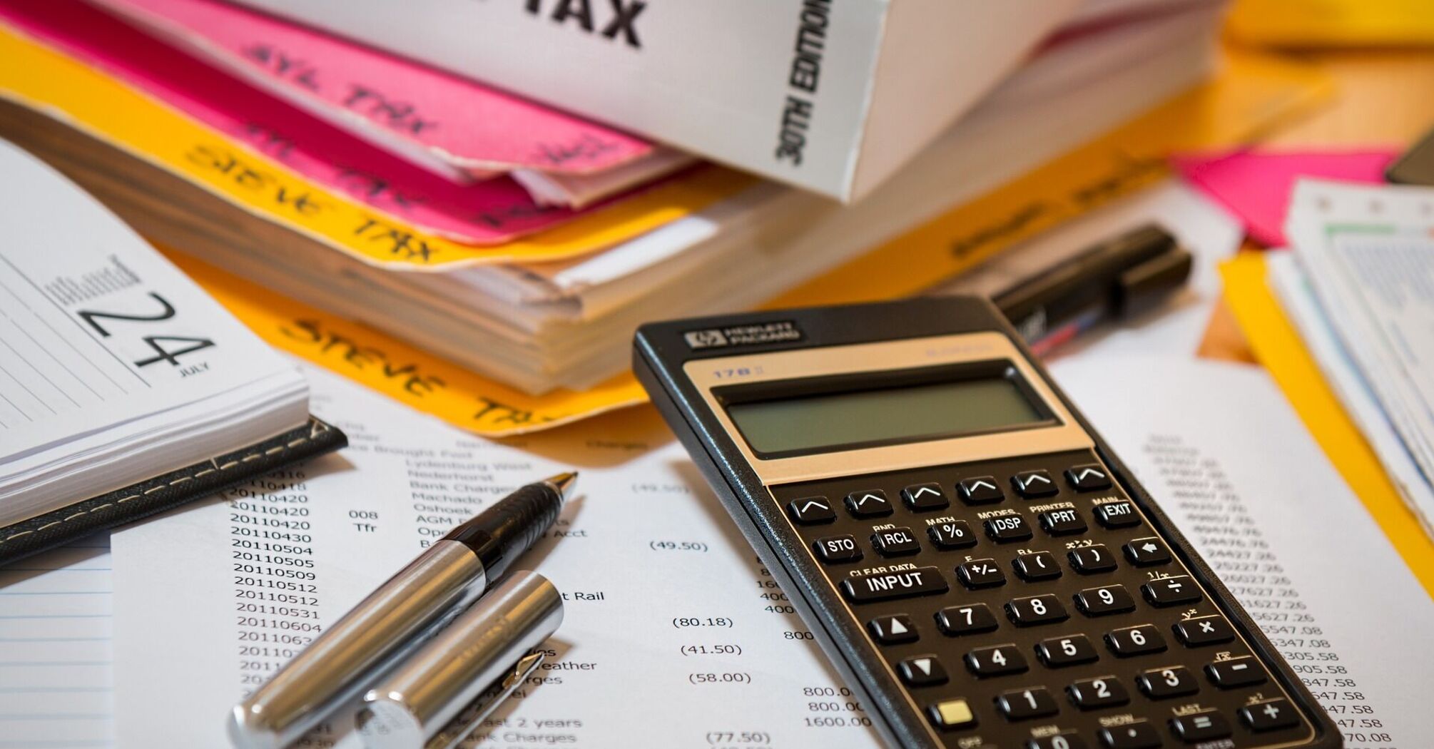 An array of income tax documents, calculator, and pens on a table