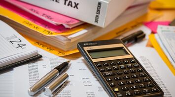 An array of income tax documents, calculator, and pens on a table