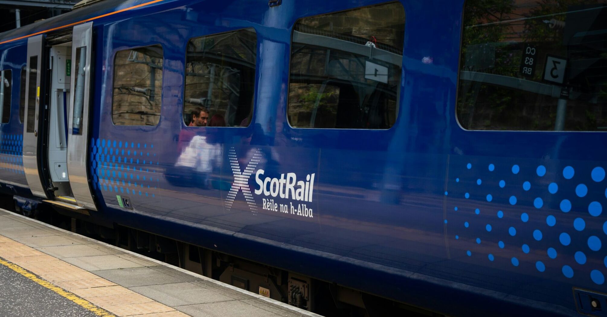 ScotRail train stopped at a station platform, doors open, with passengers visible inside