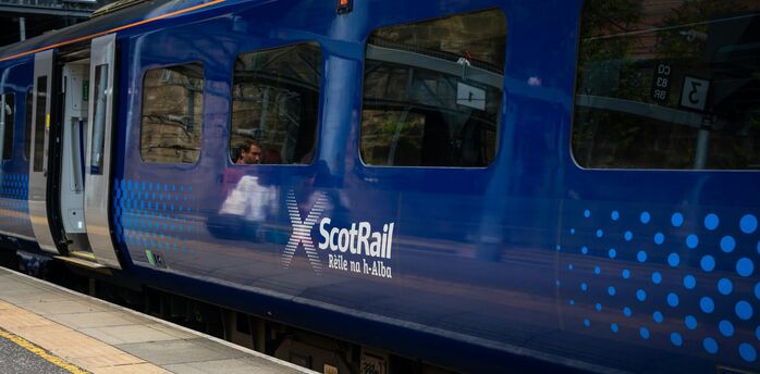 ScotRail train stopped at a station platform, doors open, with passengers visible inside