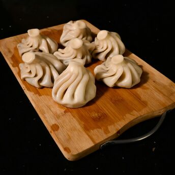 Freshly-made khinkali (a Georgian dumpling), a delicacy in Georgia, on a wooden chopping board on a kitchen table.