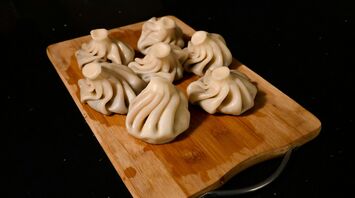 Freshly-made khinkali (a Georgian dumpling), a delicacy in Georgia, on a wooden chopping board on a kitchen table.