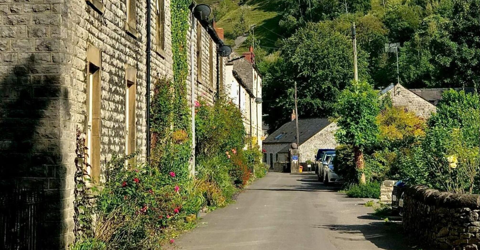 A picturesque street in a village with stone houses and a backdrop of green hills under a clear blue sky