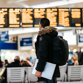 Man standing inside airport looking at led flight schedule bulletin board