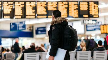 Man standing inside airport looking at led flight schedule bulletin board