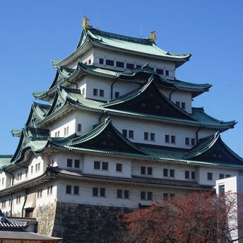 Nagoya Castle, a historic Japanese castle with green-tiled, multi-tiered roofs and golden ornaments, under a clear blue sky