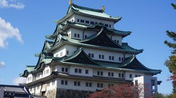 Nagoya Castle, a historic Japanese castle with green-tiled, multi-tiered roofs and golden ornaments, under a clear blue sky