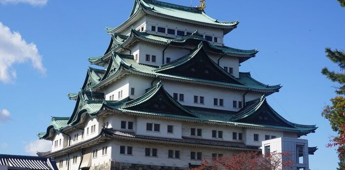 Nagoya Castle, a historic Japanese castle with green-tiled, multi-tiered roofs and golden ornaments, under a clear blue sky