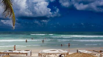 A sandy beach with people swimming in the ocean