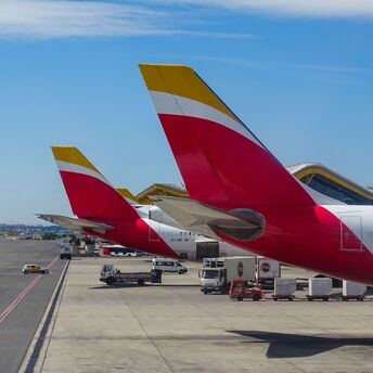Iberia aircraft tails lined up at an airport, showcasing the airline's distinctive red and yellow livery