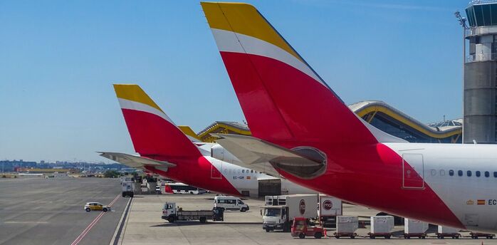 Iberia aircraft tails lined up at an airport, showcasing the airline's distinctive red and yellow livery
