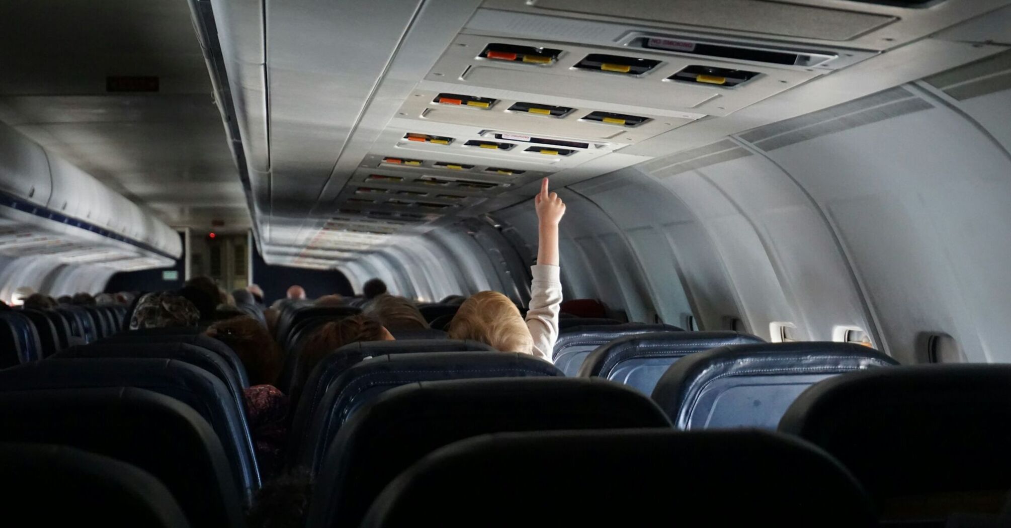 Child reaching up to overhead bins in airplane aisle