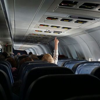 Child reaching up to overhead bins in airplane aisle