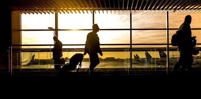 Silhouetted travelers at an airport terminal during sunset
